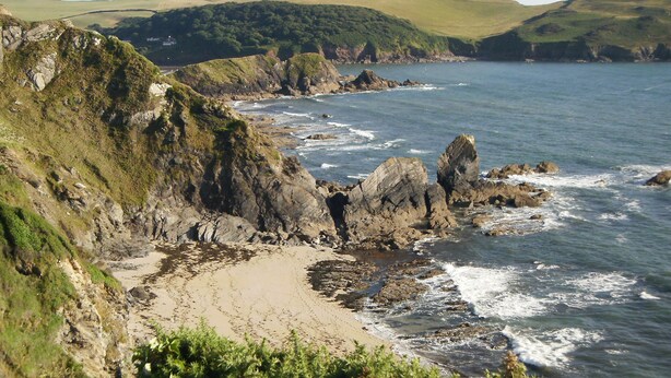 A coastal landscape with rocky cliffs, a sandy beach, and a view of the sea. - Cottage View (Kingsbridge)