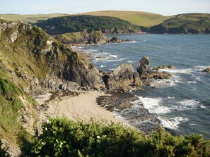 A coastal landscape with rocky cliffs, a sandy beach, and a view of the sea.