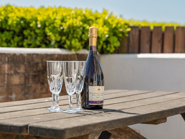 A bottle of wine and three glasses on a wooden table.