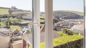 A view from a window overlooking a coastal village with houses, green hills, and a clear sky. - Cottage View (Kingsbridge)