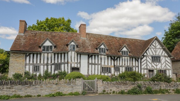 A traditional half-timbered house with a stone wall and a wooden gate.