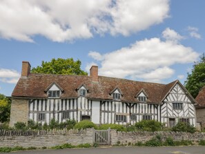 A traditional half-timbered building with a stone wall in front, under a partly cloudy sky. - 5 Albany Road (Stratford-upon-Avon)