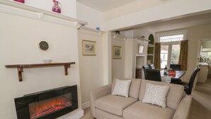 A living room with a fireplace, a sofa, a dining table, and a kitchen area in the background.