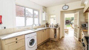 A kitchen with a washing machine, a sink, and a clock on the wall.