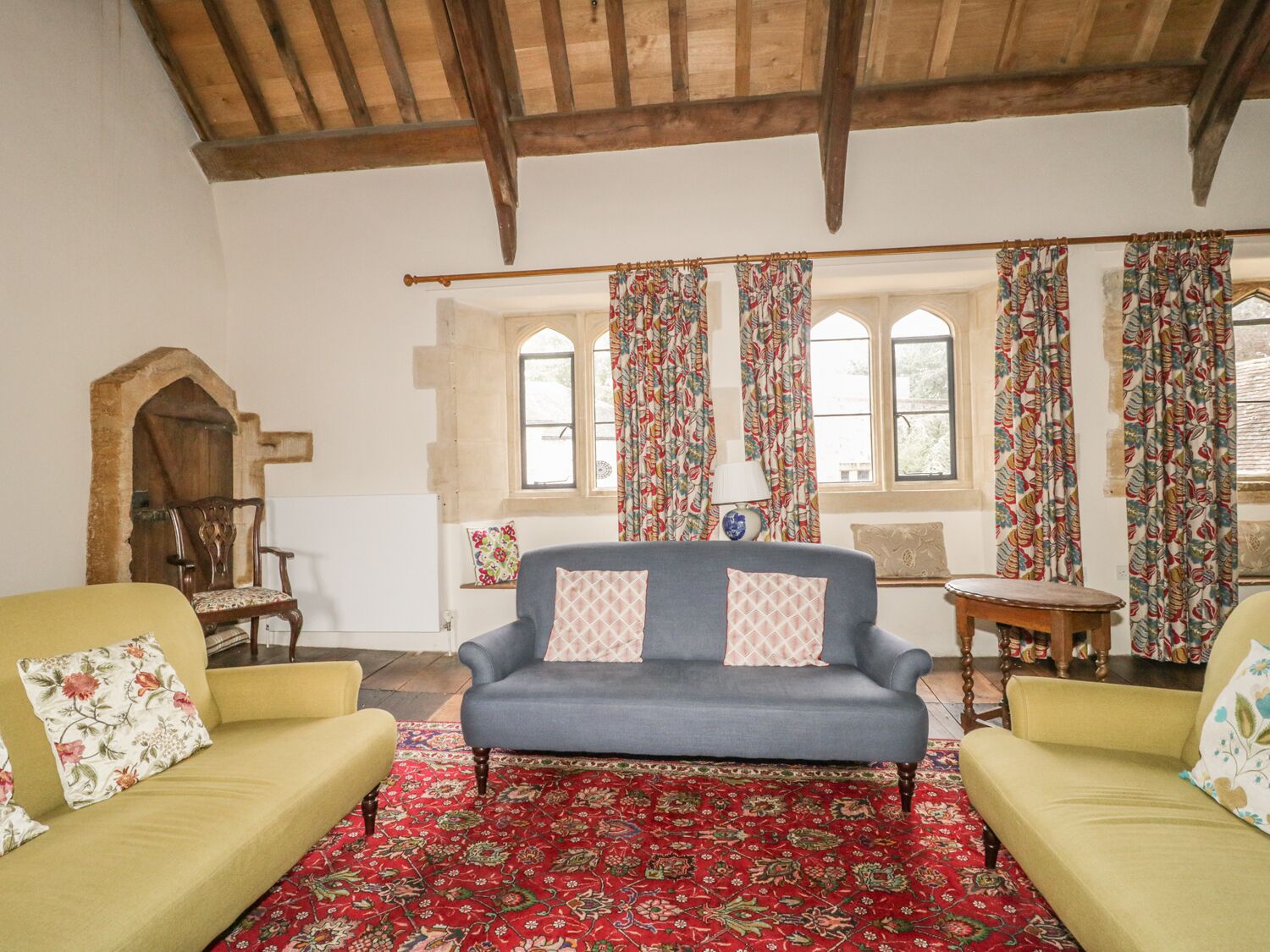 Une pièce avec un canapé bleu, deux fauteuils jaunes, un tapis rouge à motifs et un plafond en bois.
