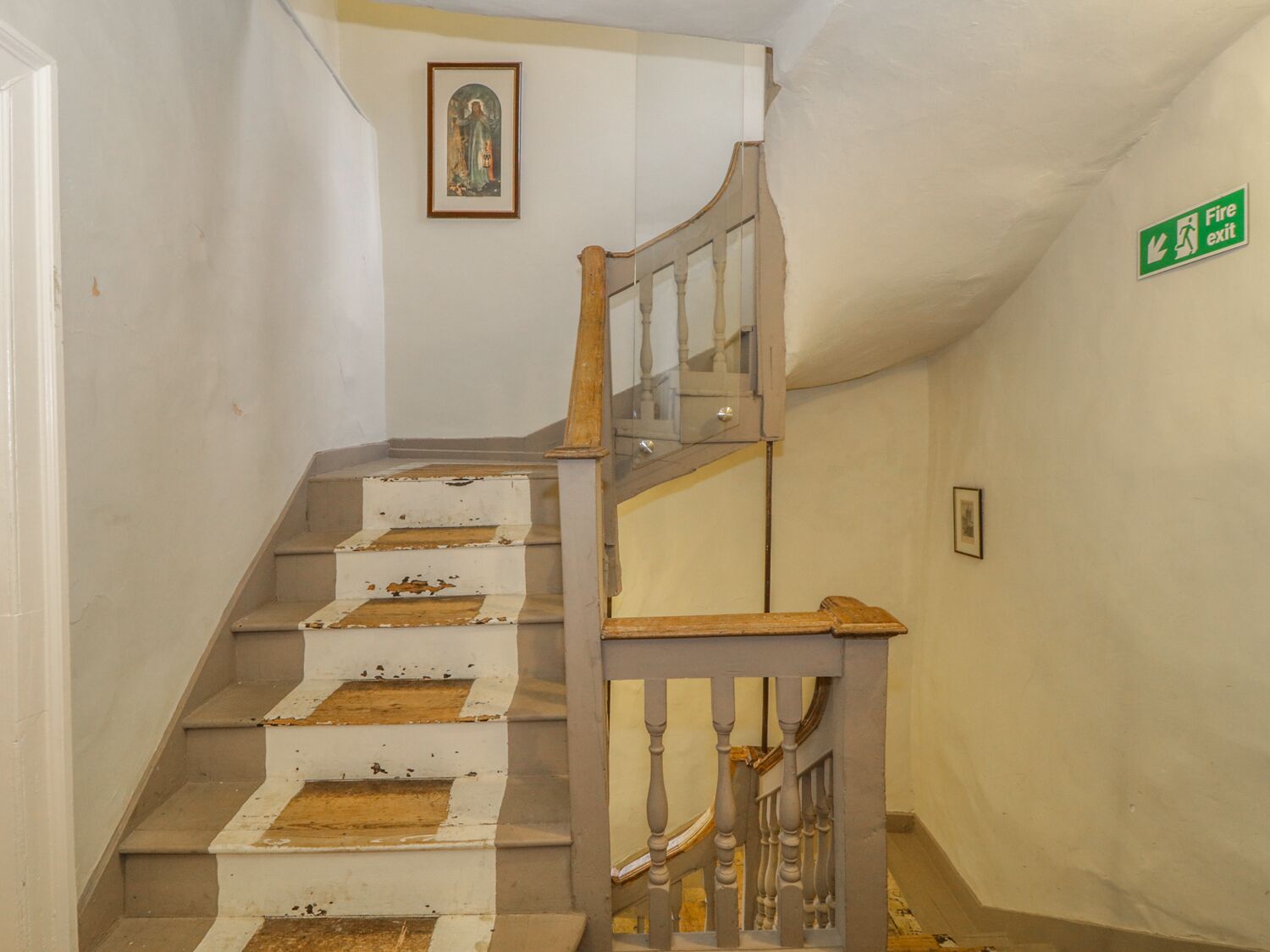 A staircase with a wooden handrail and white steps, a framed picture on the wall, and a green fire exit sign.