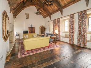 A spacious room with a high ceiling, wooden beams, a large sofa, a small table, and a patterned rug. - Castle House (Taunton)