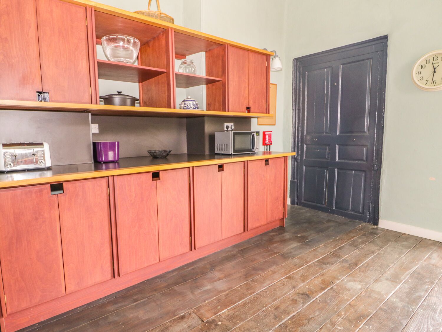 A kitchen with wooden cabinets, a microwave, a toaster, and a clock on the wall.