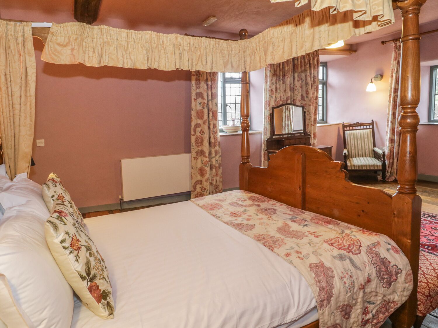 Una cama con dosel, un edredón floral, un cabecero de madera y un espejo encima.