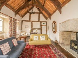 A cozy room with a wooden ceiling, a fireplace, a sofa, a patterned rug, and a table with lamps.