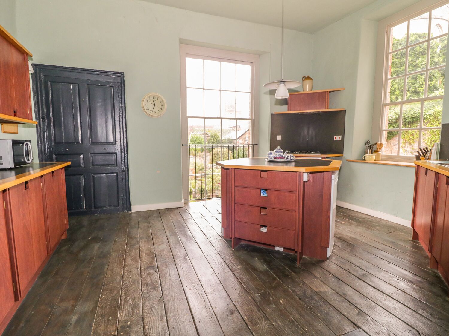 Cocina con armarios de madera, una puerta negra, un ventanal y vistas al exterior con vegetación.