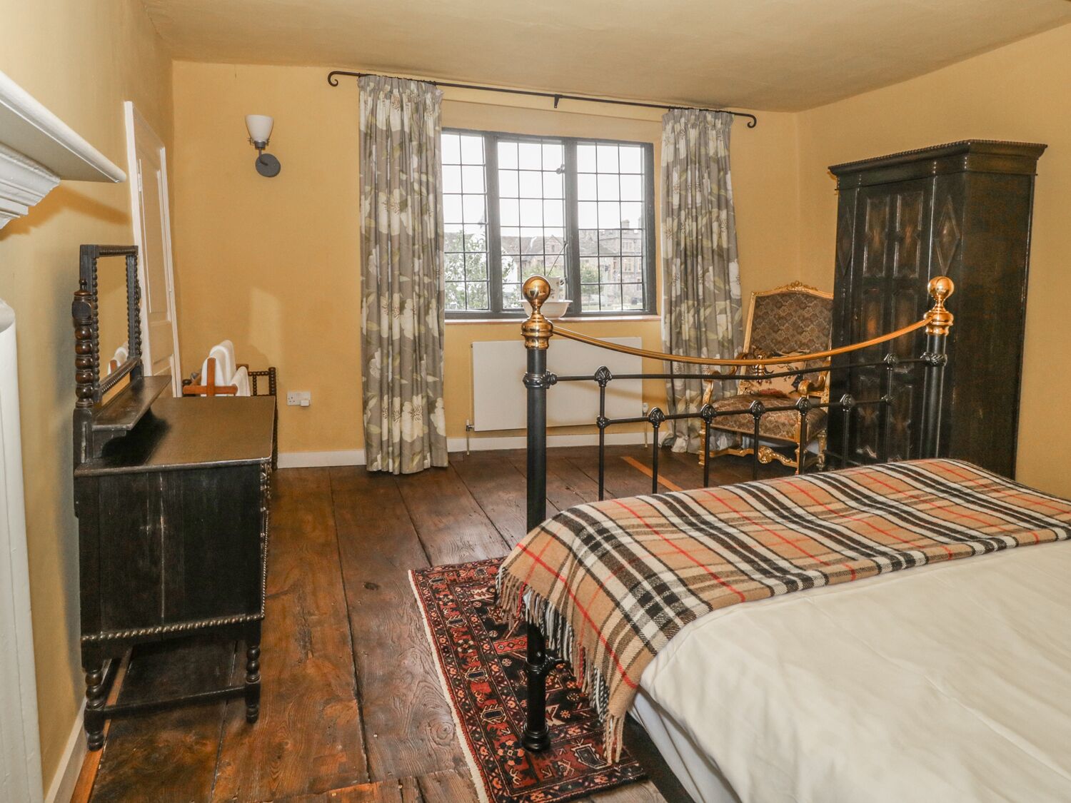 A bedroom with a bed, a dresser, a chair, a window with curtains, and a radiator.