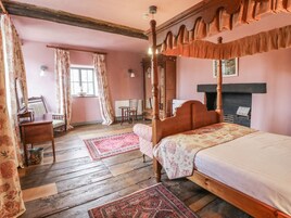 Un dormitorio tradicional con cama con dosel, suelo de madera y chimenea.