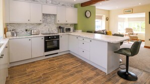 A modern kitchen with white cabinets, a marble backsplash, a built-in oven, and a wooden floor.