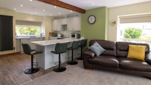 A modern kitchen with a central island, bar stools, a brown leather sofa, and a clock on the wall.