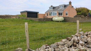 A house with a garage, a large water tank, and a stone wall.