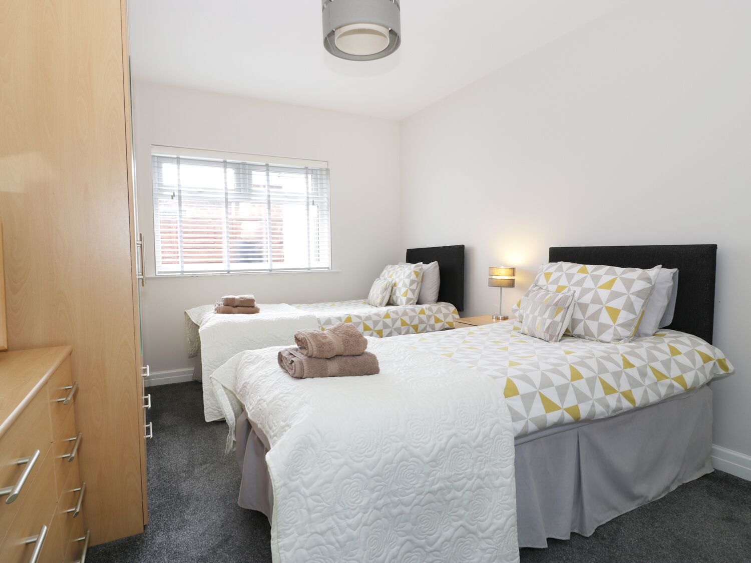 A hotel room with two beds, a wardrobe, a window with blinds, and a bedside lamp.