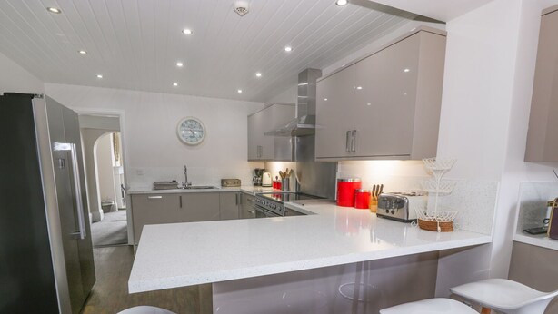 Una cocina moderna con una isla central, taburetes de bar, electrodomésticos de acero inoxidable y un reloj en la pared.