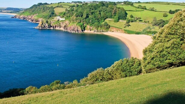 A coastal landscape with a sandy beach, grassy hills, and a clear blue sea. - Leeside (Dartmouth)