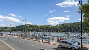 A marina with boats docked, a road with a car, and a hilly landscape in the background. - Leeside (Dartmouth)