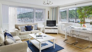 A modern living room with a sofa, coffee table, TV, and dining area with chairs and a table. - Leeside (Dartmouth)