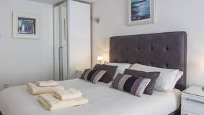 A neatly made bed with a grey headboard, white bedding, and striped pillows. There are two folded towels on the bed. A nightstand with a lamp is to the right. - Leeside (Dartmouth)