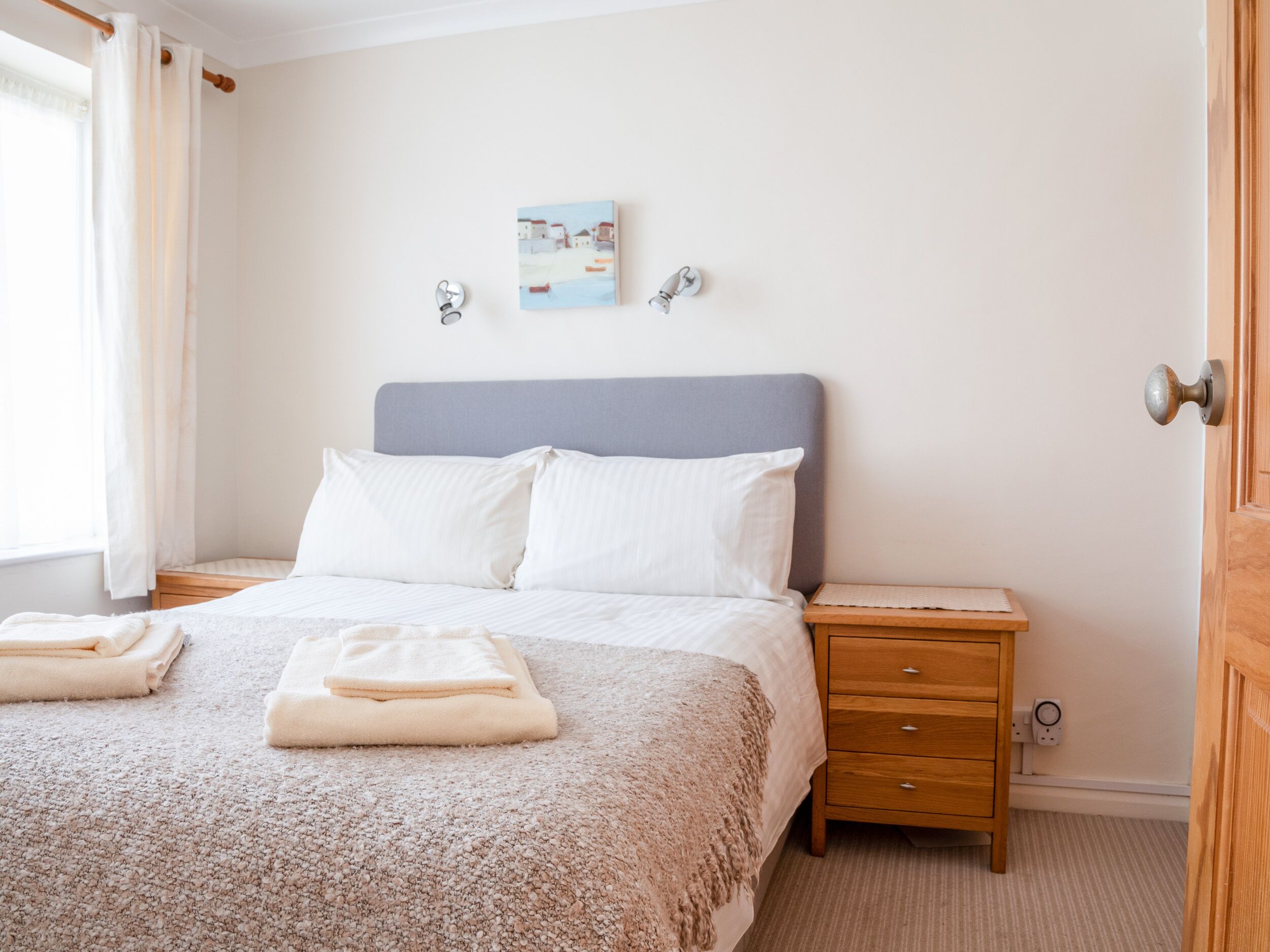 A bedroom with a bed, two bedside tables, a nightstand, a painting on the wall, and a door.