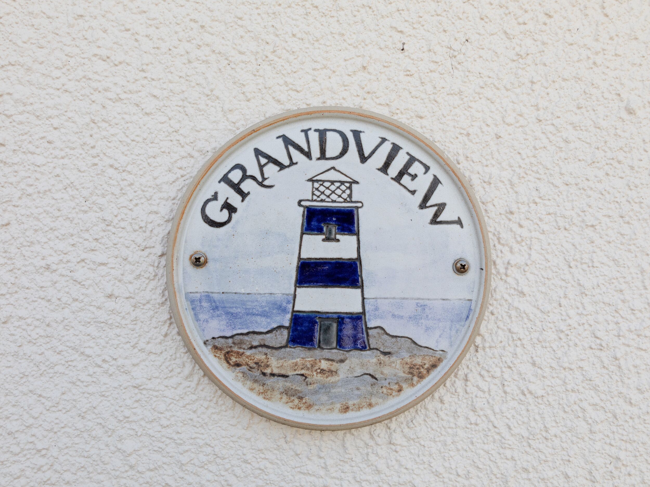 A circular sign with a lighthouse illustration and the word "GRANDVIEW" on a textured wall.