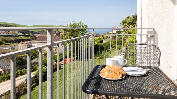 A balcony with a table set for two, overlooking a coastal landscape. - Grand View (Kingsbridge)