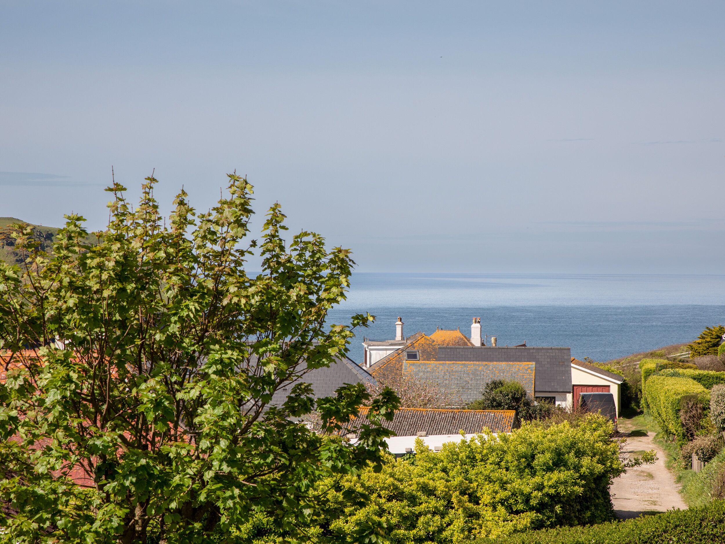 A coastal property with a view of the sea, surrounded by lush greenery and a clear sky.