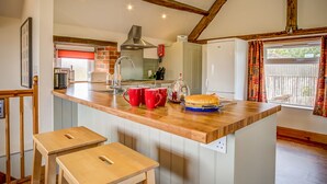 A kitchen with a wooden island, a built-in oven, and a refrigerator. There are two stools and a window with curtains. - Top Barn (Shipston on Stour)