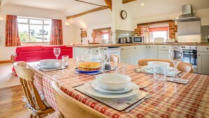 A dining area with a table set for four, a red sofa, and a kitchen in the background. - Top Barn (Shipston on Stour)