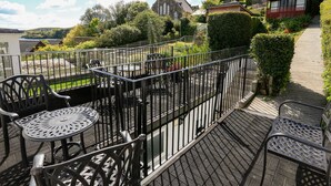 Una terrazza con tavoli e sedie in metallo, un edificio in pietra sullo sfondo e un sentiero che conduce a una casa.