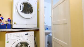 A laundry room with two stacked washing machines, a sink, and cleaning supplies.