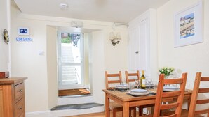 Zona pranzo con tavolo di legno apparecchiato per quattro, una finestra vista esterna e una porta che conduce a una scala.