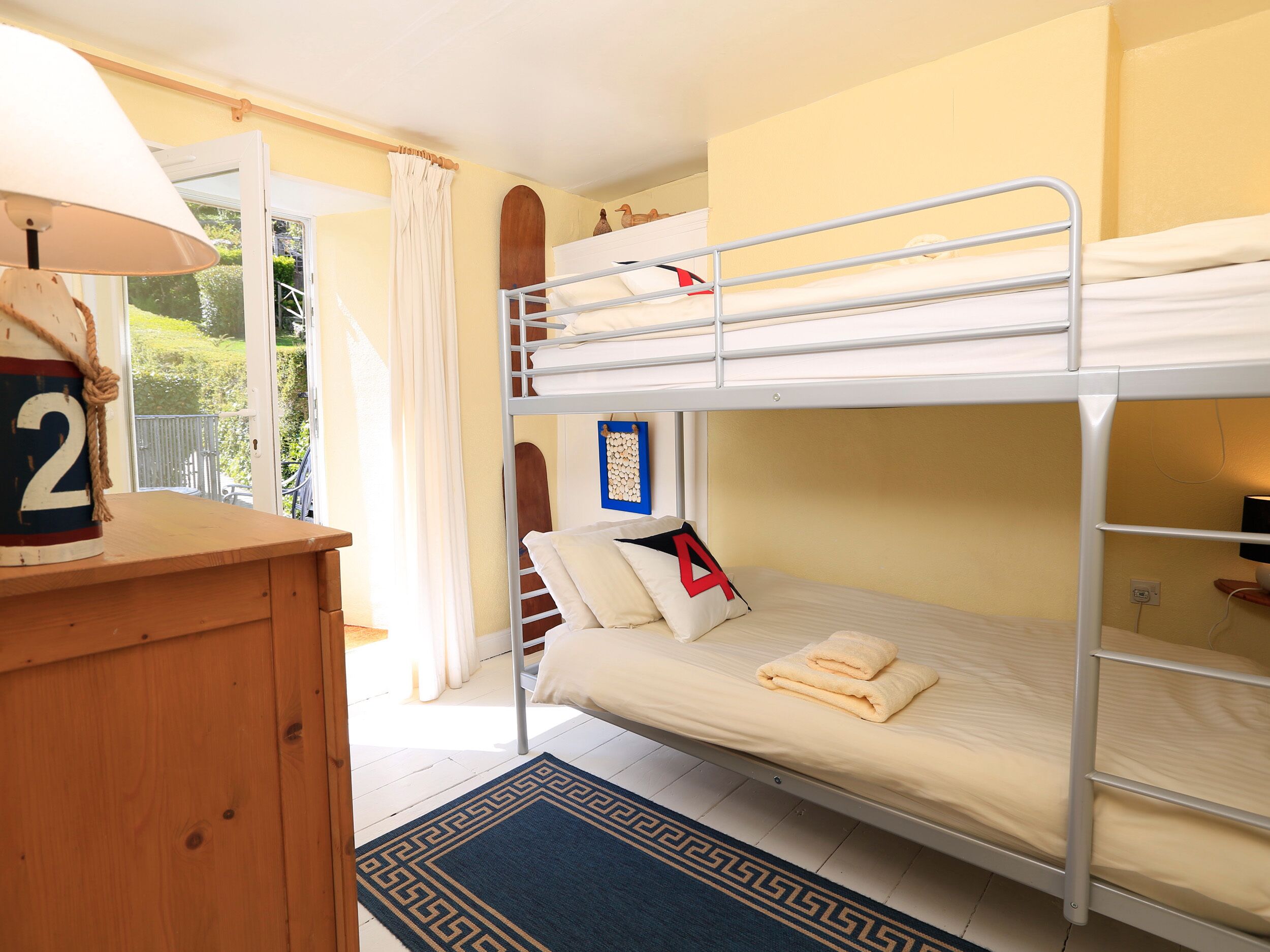 A bunk bed room with a wooden desk, a lamp, and a view of the outdoors.