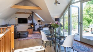 Un vaste espace de vie comprenant une table à manger en verre, des sièges confortables, une cheminée et une grande fenêtre donnant sur l’extérieur.