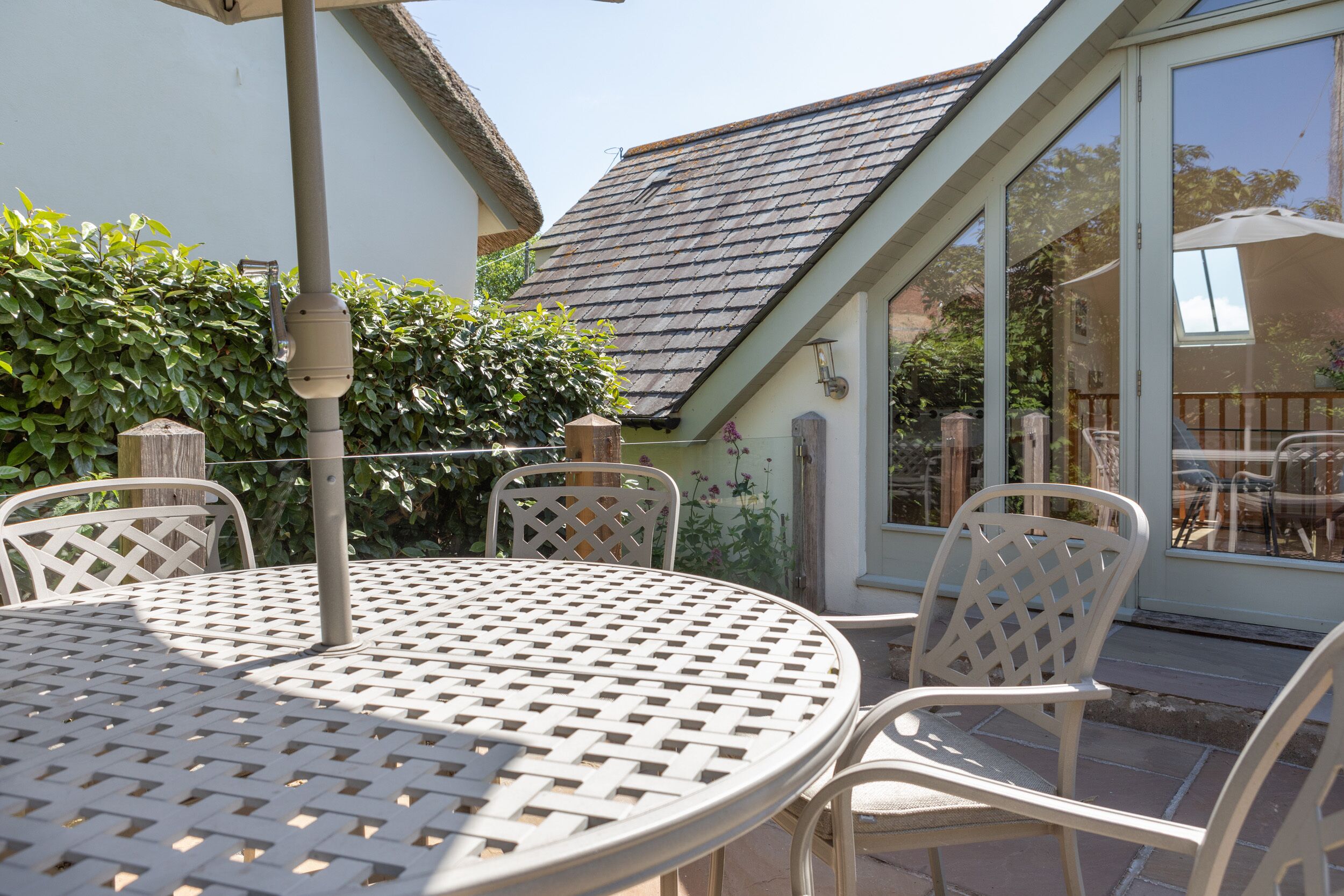 A patio with a round table and white chairs, a pergola, and a view of a house with a sloped roof.