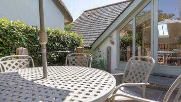 A patio with a round table and white chairs, a pergola, and a view of a house with a sloped roof.