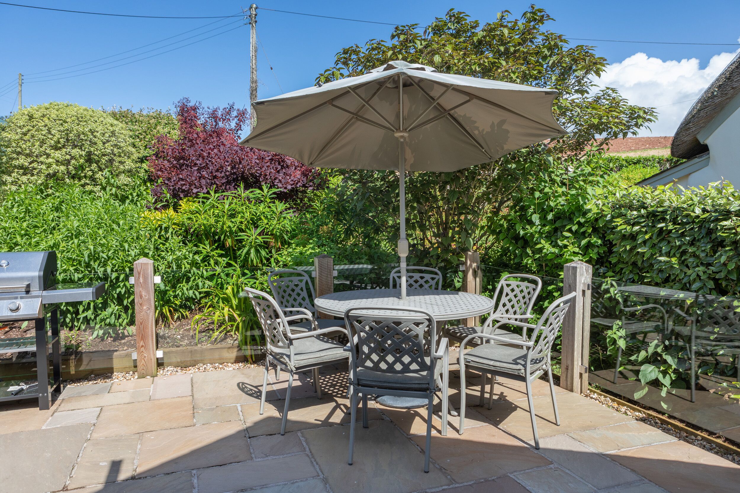 An outdoor patio with a round table and chairs, a grill, and an umbrella.