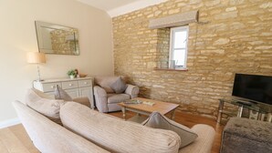 A living room with a stone wall, a sofa, a coffee table, a TV, and a lamp. - Ewecub Barn (Witney)