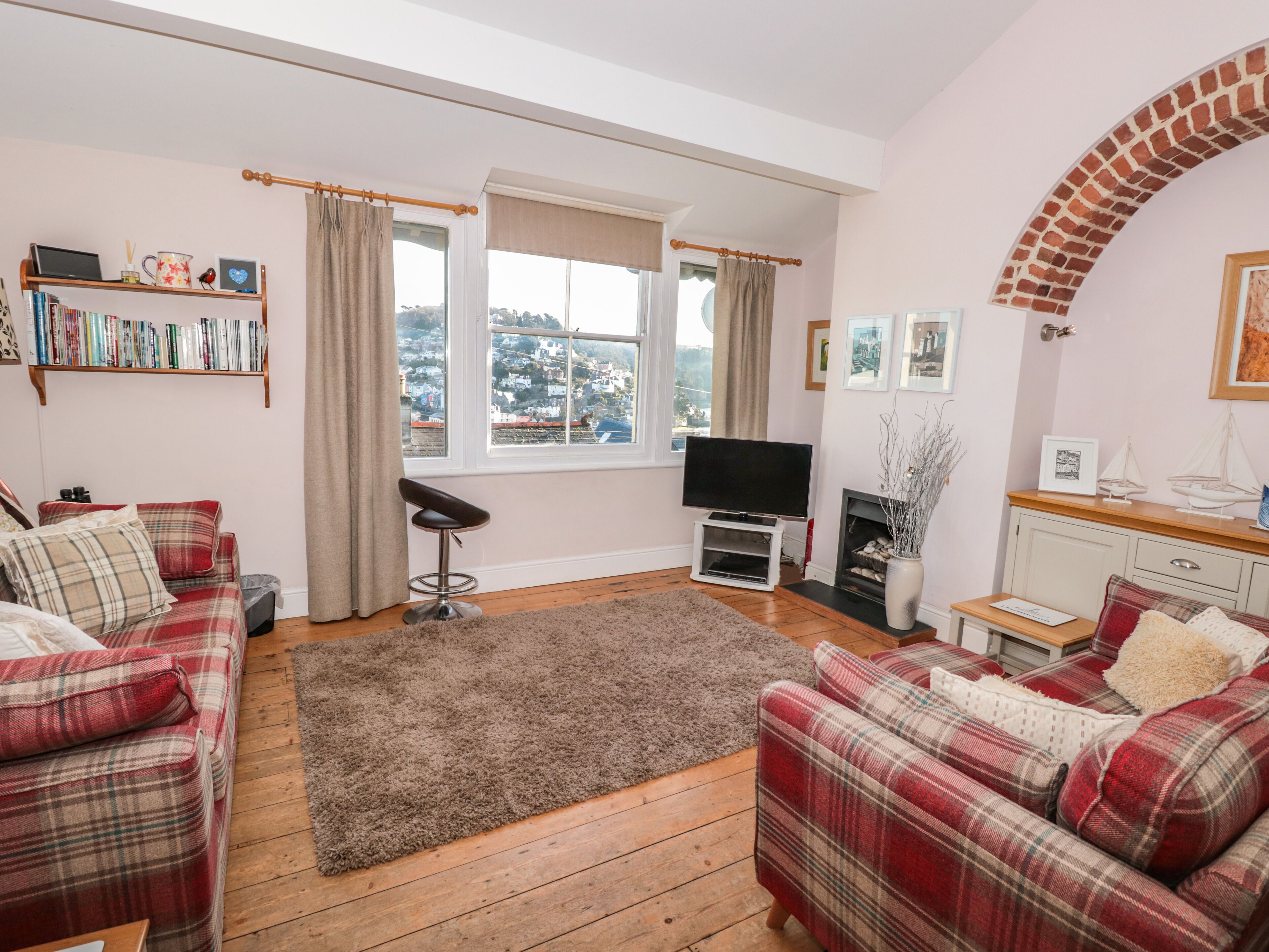A cozy living room with two plaid sofas, a TV, a fireplace, and a bookshelf.