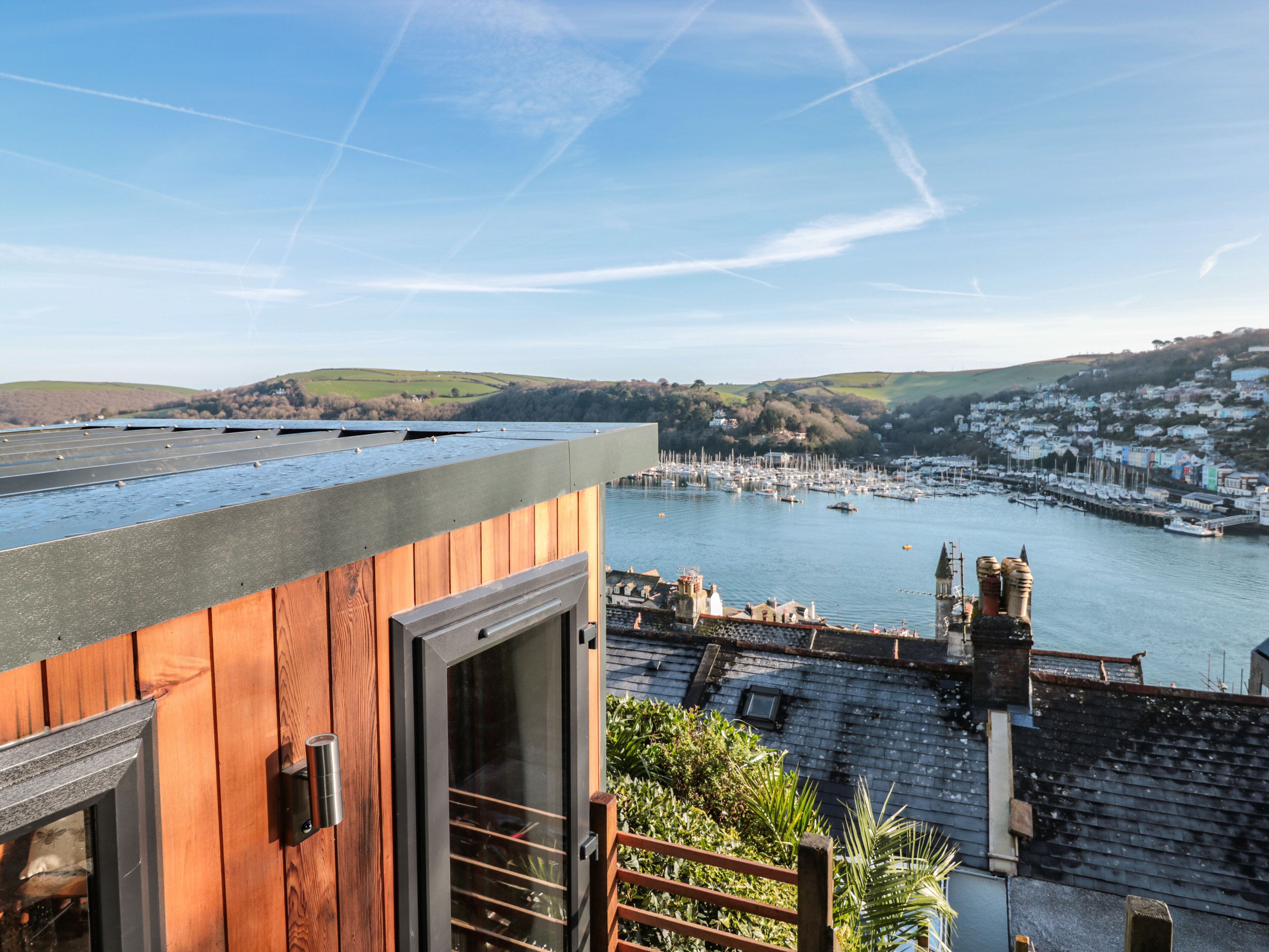 A view from a wooden balcony overlooking a marina with boats, a town in the background, and a clear sky.