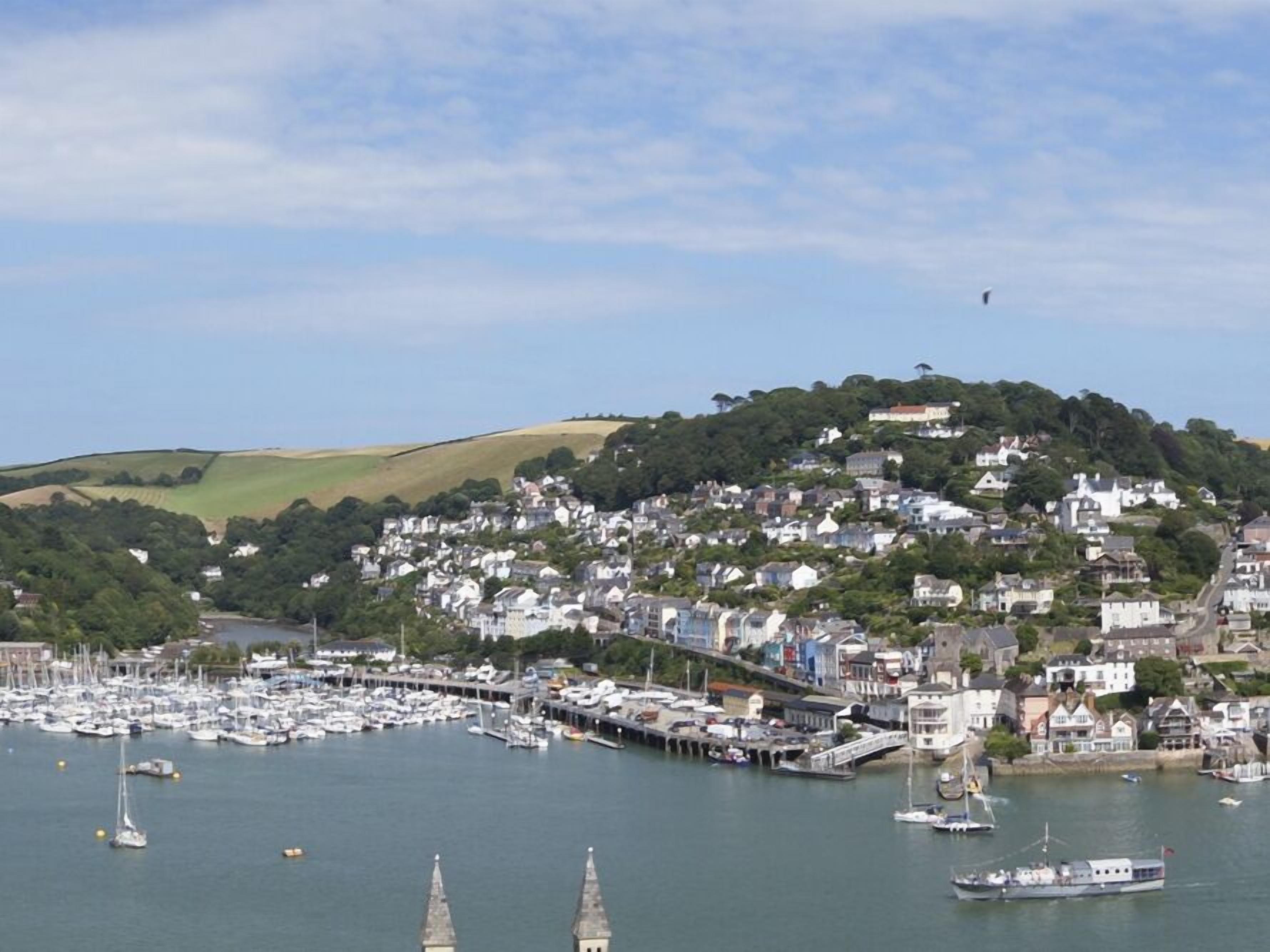 A coastal town with a marina filled with boats, a hilltop with buildings, and a clear sky.
