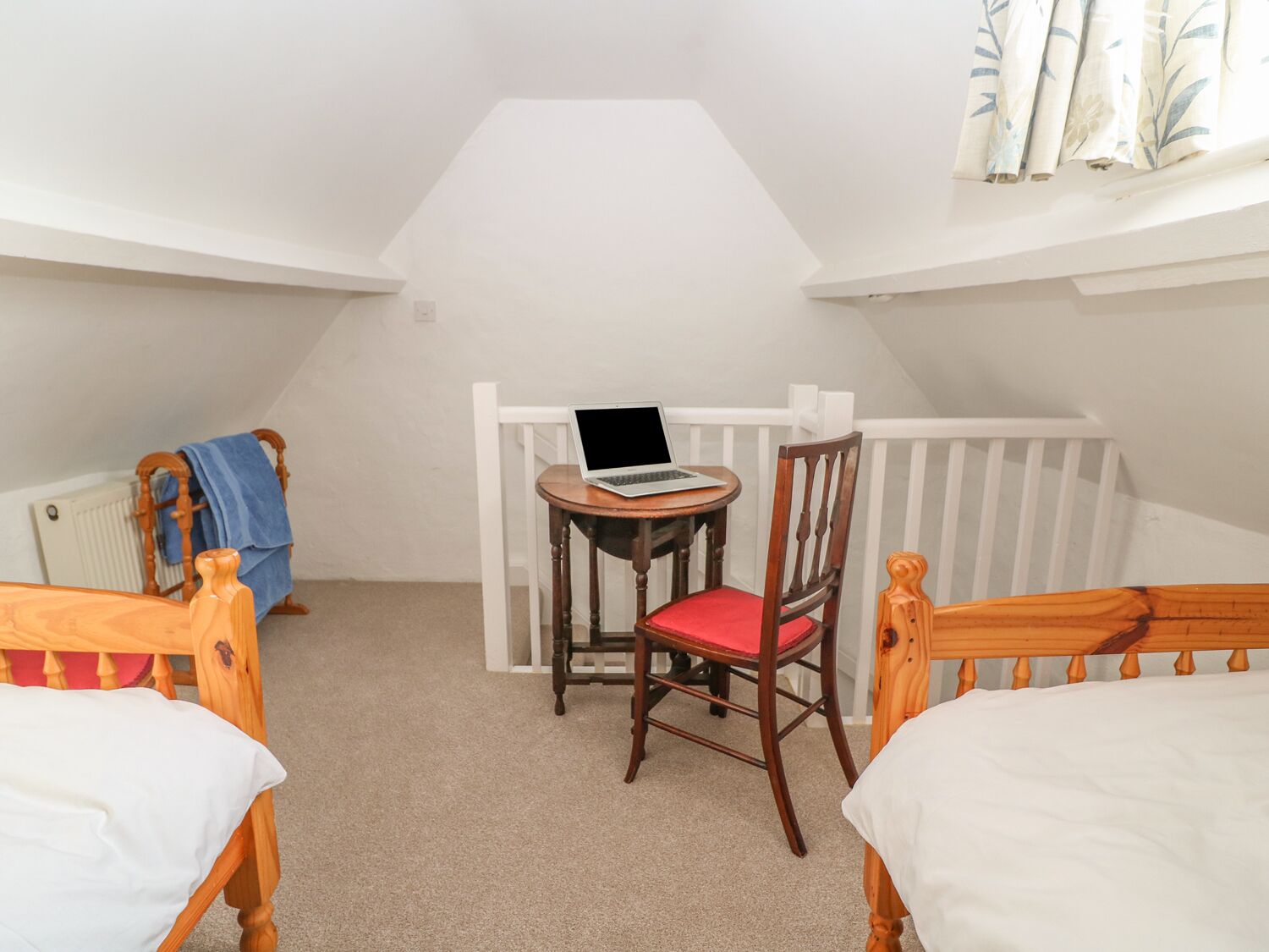 Un dormitorio de ático pequeño y acogedor, con una cama individual, una silla y un ordenador portátil sobre una mesa.