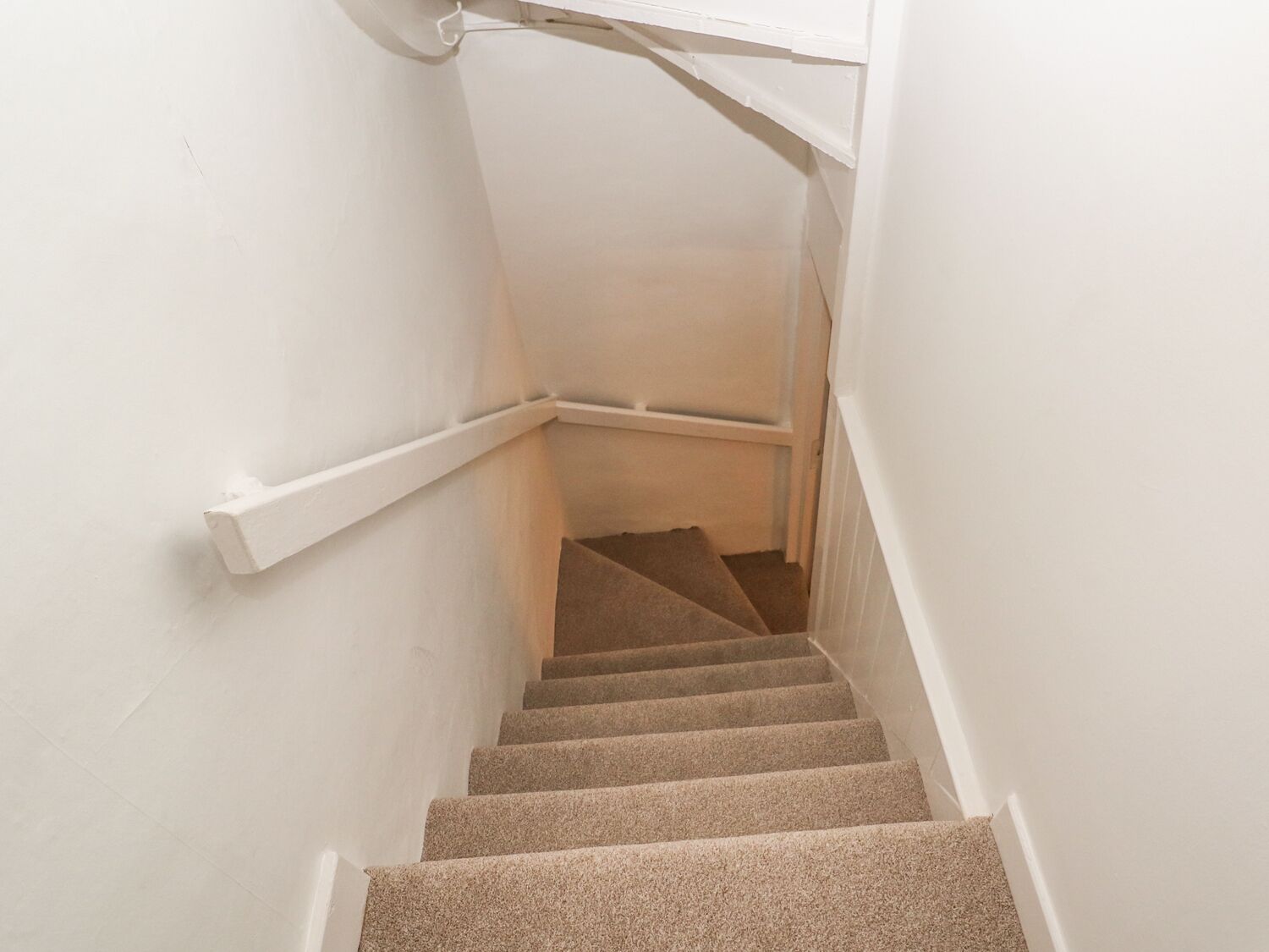 Un escalier recouvert de moquette, avec des murs blancs et une main courante.