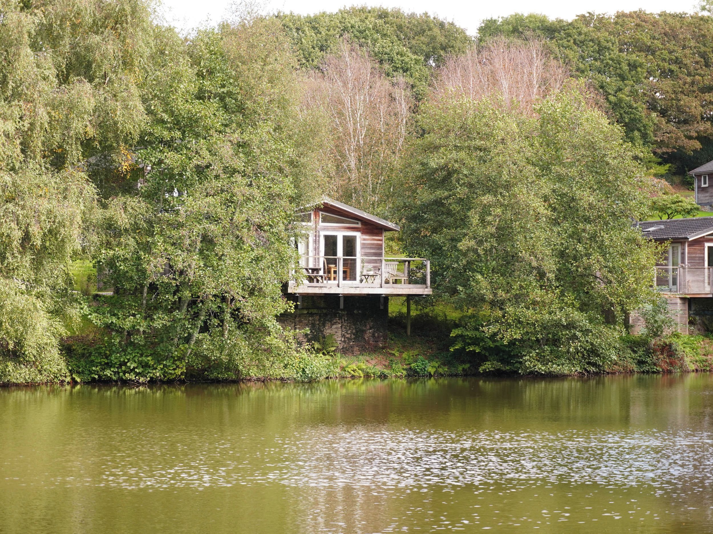 A cabin with a deck overlooking a lake, surrounded by dense foliage.