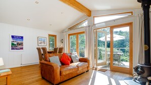 A spacious living room with a leather sofa, wooden flooring, and large windows offering a view of the outdoors. - 2 Water's Edge (Looe)