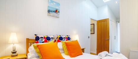 A bedroom with a bed, pillows, a nightstand, a lamp, a painting, a wooden door, and towels.