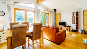 A spacious living room with a wooden ceiling, a fireplace, a television, and a dining area with chairs and a table. - 2 Water's Edge (Looe)